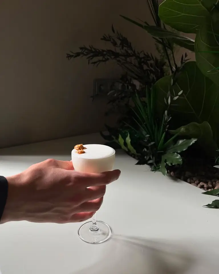 A cocktail held up against the dark greenery